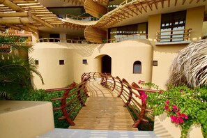 A wooden pathway leading to a building with multiple balconies and a thatched roof structure. - KauKan A2 Luxury Condo with Breathtaking View (Zihuatanejo)