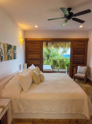 A bedroom with a bed, pillows, a ceiling fan, and a view of the outdoors.