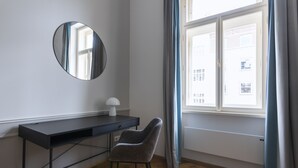Habitación con escritorio, silla, espejo redondo y ventana con cortinas.