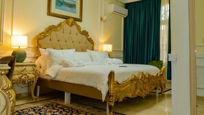 A hotel room with a large bed, ornate headboard, two bedside lamps, a framed picture on the wall, and a window with curtains. - Hôtel Chateau Blanc  (Yamoussoukro)