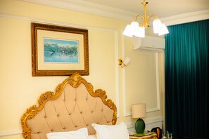 A hotel room with a tufted headboard, a framed painting, an air conditioning unit, and a green curtain. - Hôtel Chateau Blanc  (Yamoussoukro)