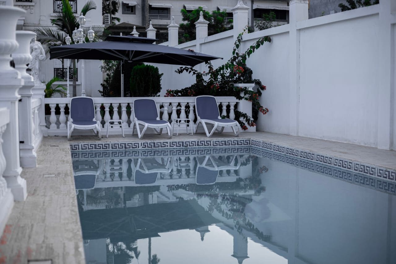 Un área de piscina con balaustradas blancas, un paraguas negro y dos sillas de descanso.
