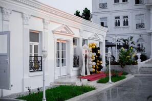A white building with a red carpet, a balcony with black railings, and a staircase leading to a door.