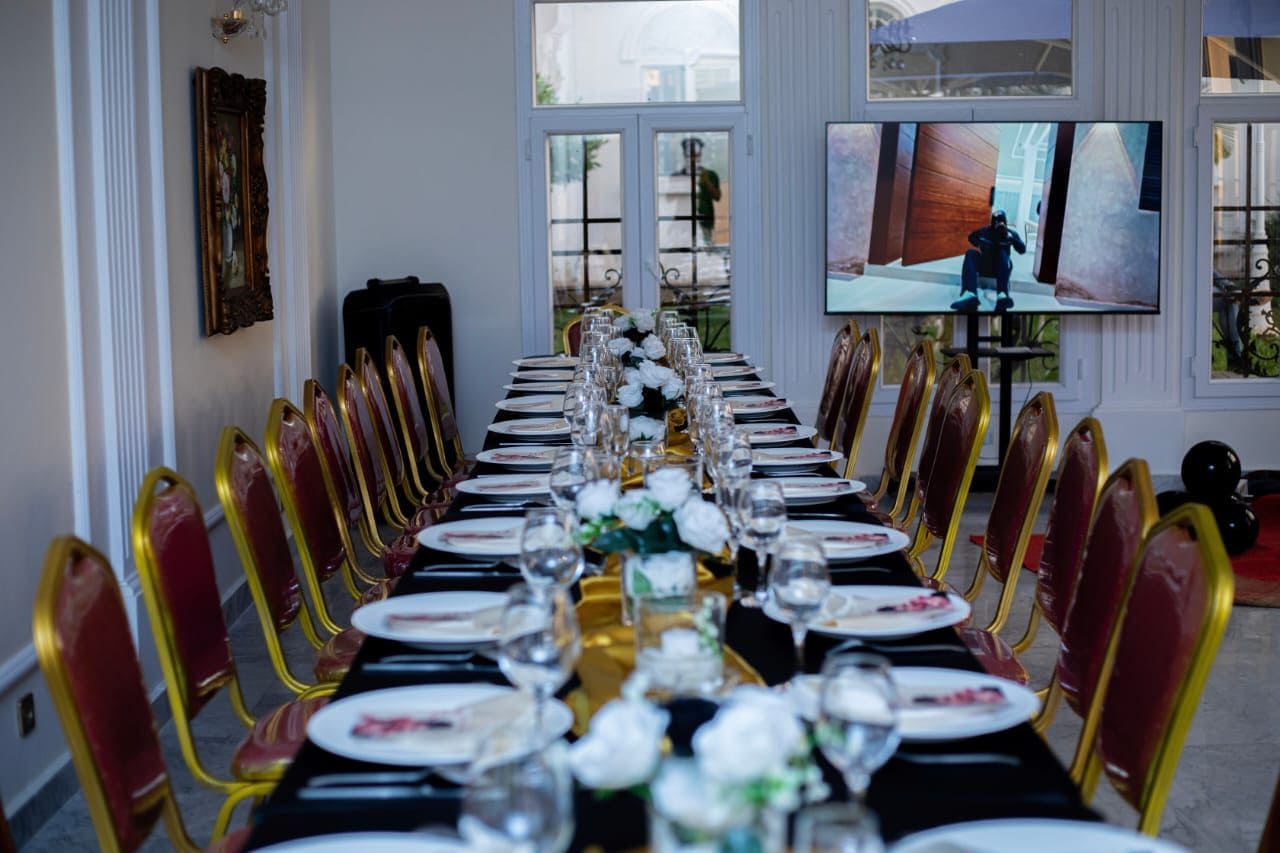 A long dining table set for a formal event with chairs, a television screen, and a framed picture on the wall.