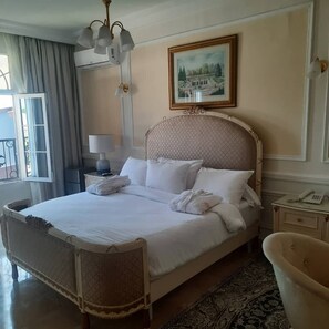 A hotel room with a large bed, a bedside table with a lamp, a painting on the wall, and a view of the outside. - Hôtel Chateau Blanc  (Yamoussoukro)