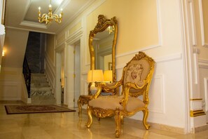 Un fauteuil doré et richement décoré, assorti à un miroir et à une lampe, un escalier en marbre et un lustre dans un hall bien éclairé.