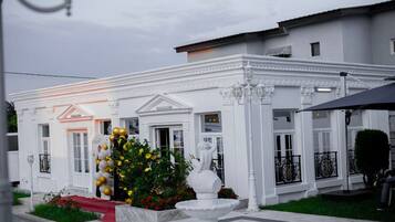 Um edifício branco com um tapete vermelho que leva à entrada, uma fonte e um jardim bem cuidado.