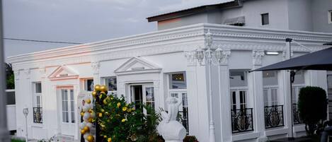 A white building with a red carpet leading to the entrance, a fountain, and a well-maintained garden.