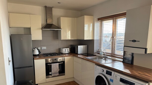 A compact kitchen with a washing machine, a stove, a toaster, and a sink. - Comfortable, modern 2 bed apartment in the heart of the Old Town (Hemel Hempstead)