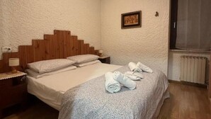 Een slaapkamer met een houten hoofdbord, een bed met witte lakens, een nachtkastje met een lamp en een raam met gordijn.