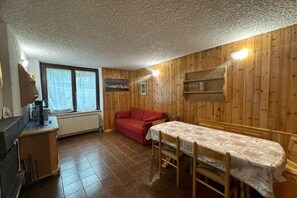 Quarto com paredes de madeira, um sofá vermelho, uma mesa de jantar com cadeiras, um radiador e uma janela com cortinas.