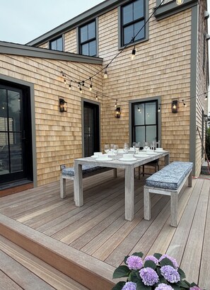 A wooden deck with a table set for dining, outdoor lighting, and a bench.