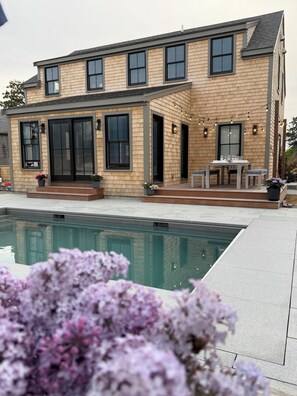 A two-story house with a swimming pool, outdoor seating, and a large window.