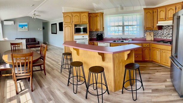 Een moderne keuken met houten kastjes, een centraal eiland met krukken, een koelkast en een eetgedeelte met stoelen en een tafel.