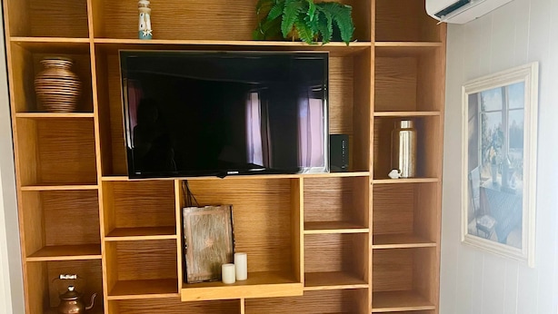 A living room with a TV, wooden shelves, a bench, and a ceiling light.