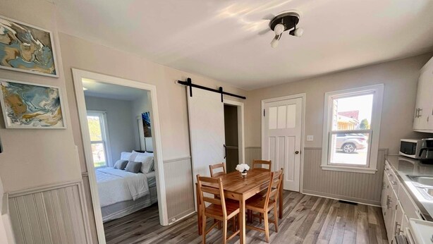 A room with a bed, a dining table with chairs, a kitchen area with a microwave, and a window with a view of the outside.