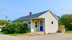 A single-story house with a blue door, a small porch, and a chimney.