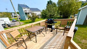 A deck with wooden furniture, a grill, and a water cooler.