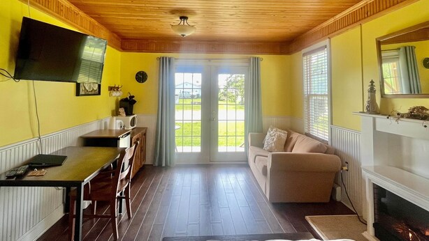 A room with a wooden ceiling, a television mounted on the wall, a sofa, a fireplace, and a dining area with a table and chairs.