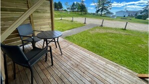 A wooden deck with a table and chairs, a covered seating area, and a view of a grassy area with trees and a clear sky.