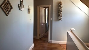 Un couloir doté d’un plancher en bois, d’un plafond en pente et d’un escalier.