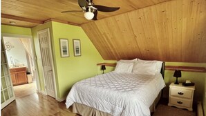 Une chambre avec un plafond en bois, un lit, une table de chevet et une porte.