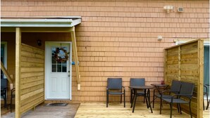 Une terrasse en bois avec des sièges d’extérieur, une porte ornée d’une guirlande de bienvenue et un mur en briques.