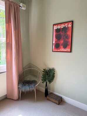 A corner room with a window, a radiator, a framed poster, a chair, a plant, and a box labeled 'CHOCOLAT REVILLON'. - One bed flat five mins from tube, Islington (London)
