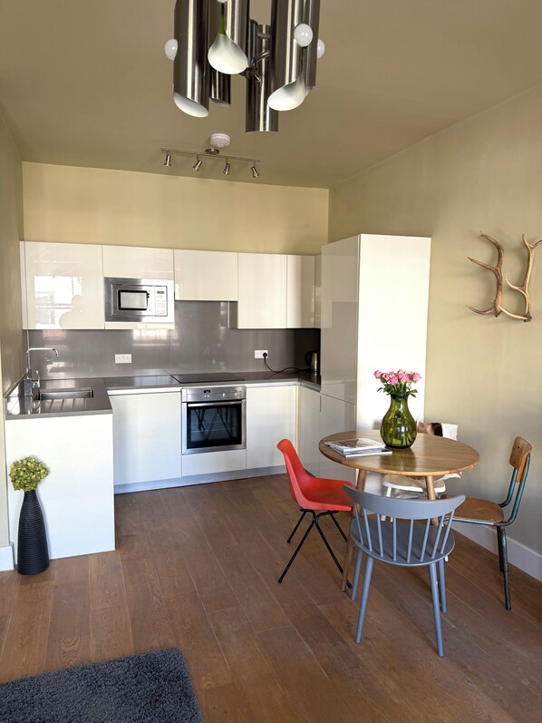 A modern kitchen with white cabinets, stainless steel appliances, and a dining area with a round table and chairs. - One bed flat five mins from tube, Islington (London)