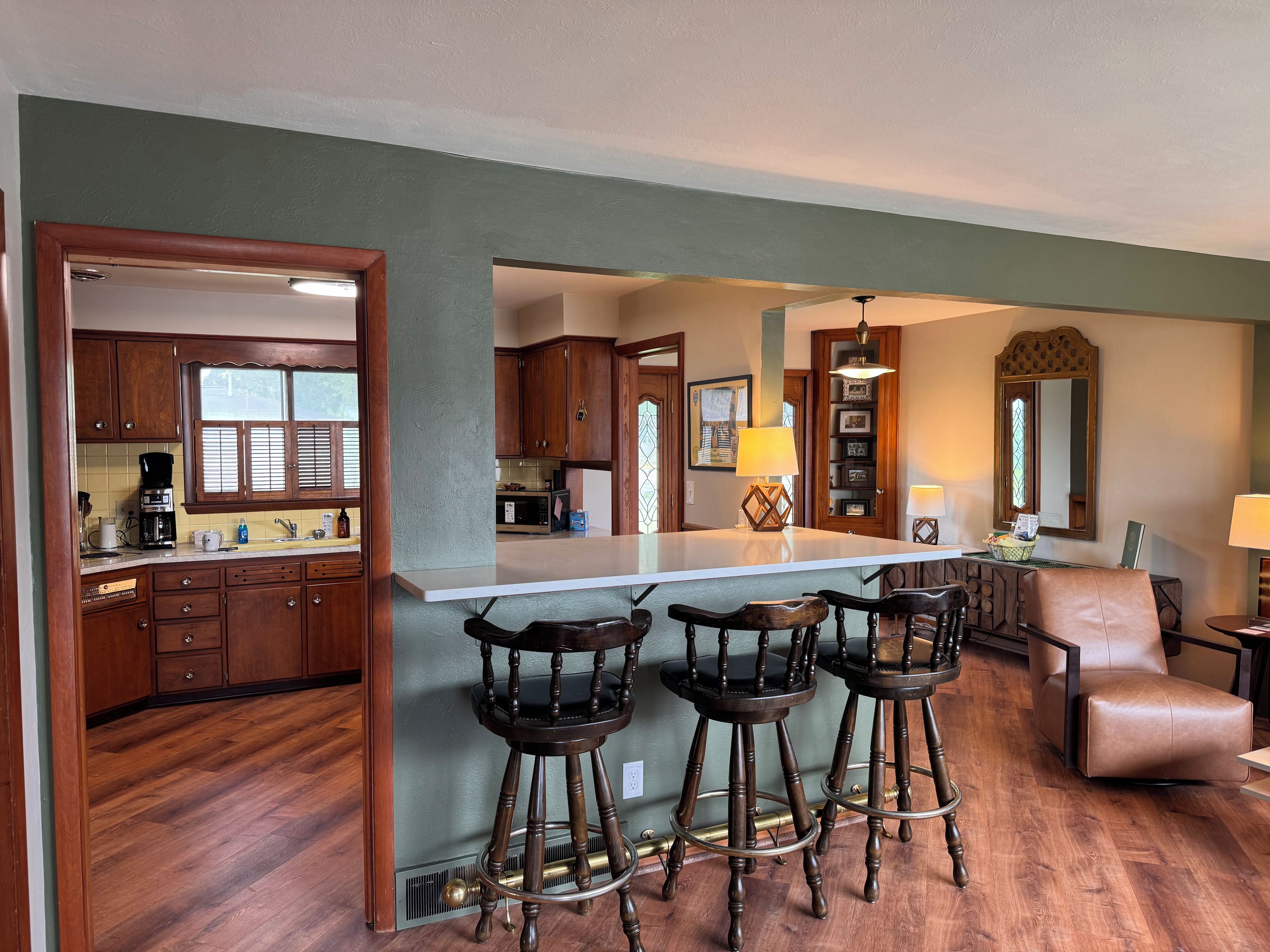 A kitchen with wooden cabinets, a central island with stools, and a dining area with a leather chair.