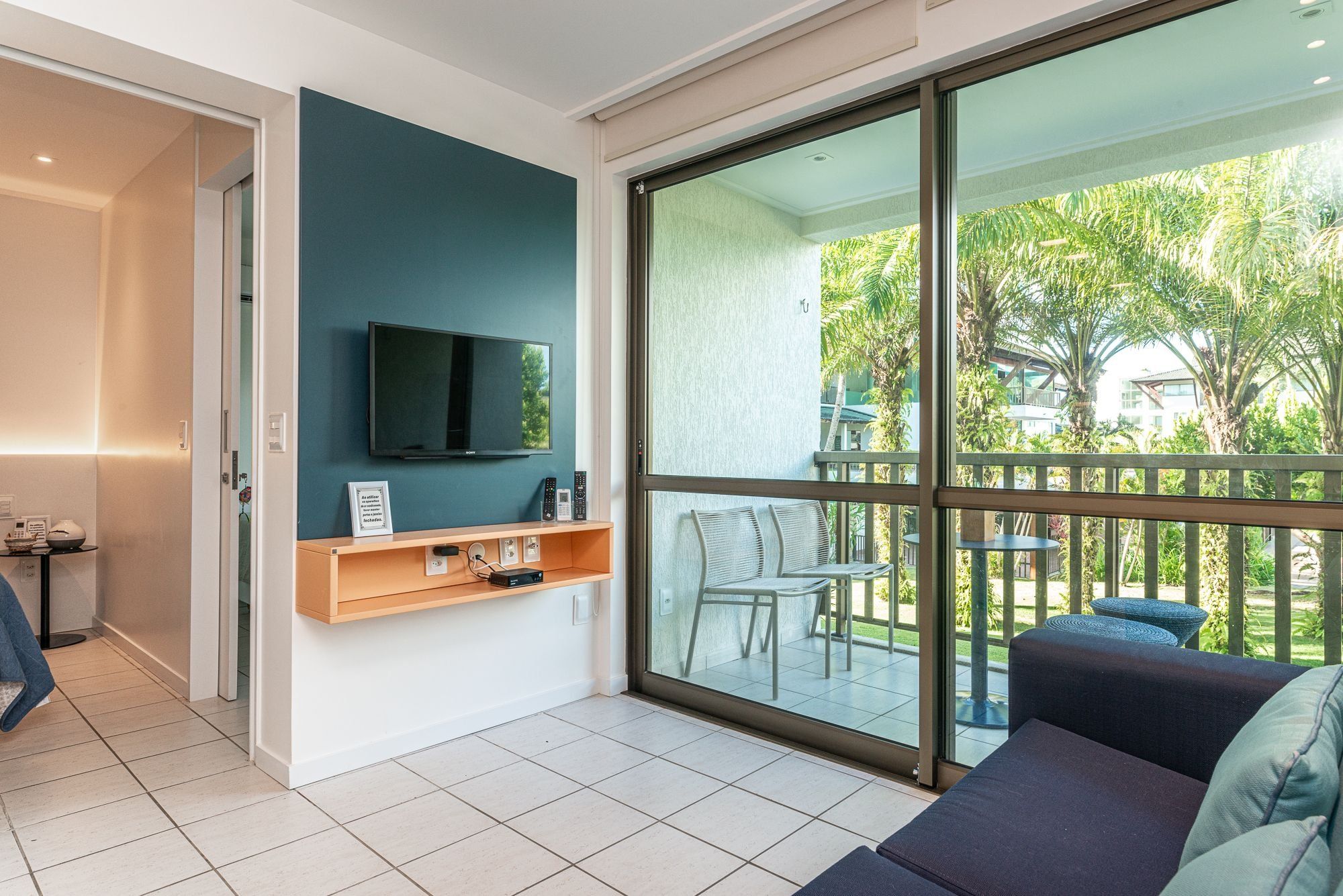 Uma sala de estar moderna com televisão de tela plana, sofá e varanda com mobiliário de exterior.