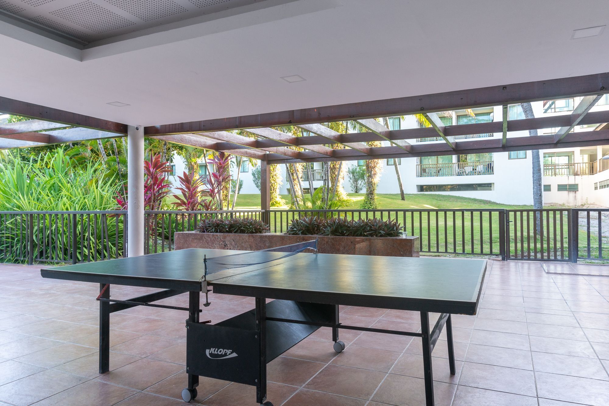 A ping pong table in a covered outdoor area with a view of a building and greenery.