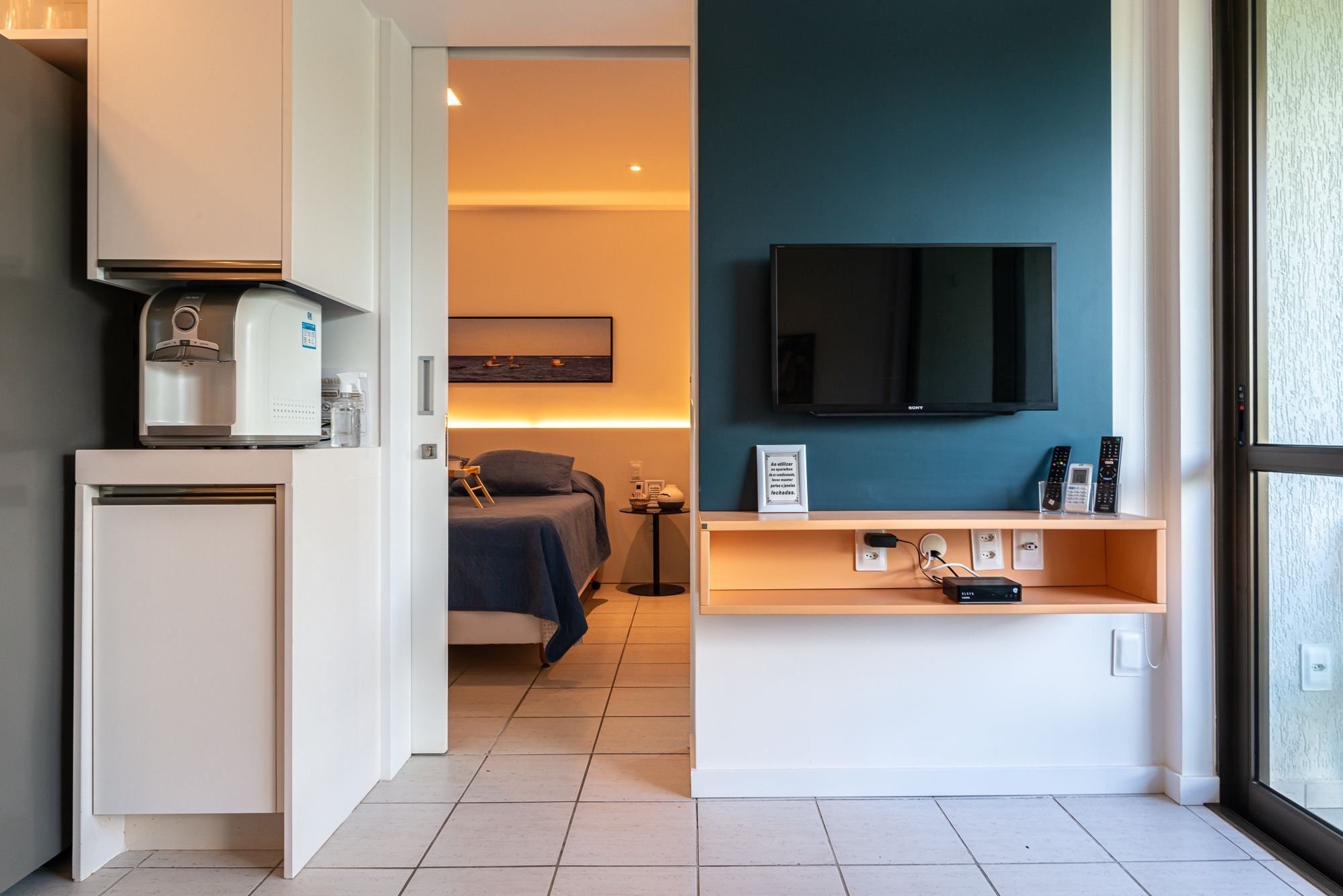 Ein Hotelzimmer mit Küchenzeile, einem Bett, einem Fernseher und einem Nachttisch mit Telefon und Fernbedienungen.