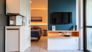Ein Hotelzimmer mit Küchenzeile, einem Bett, einem Fernseher und einem Nachttisch mit Telefon und Fernbedienungen.