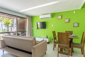 Una sala de estar con sofá, mesa de comedor, sillas, televisión de pantalla plana y una pared verde.
