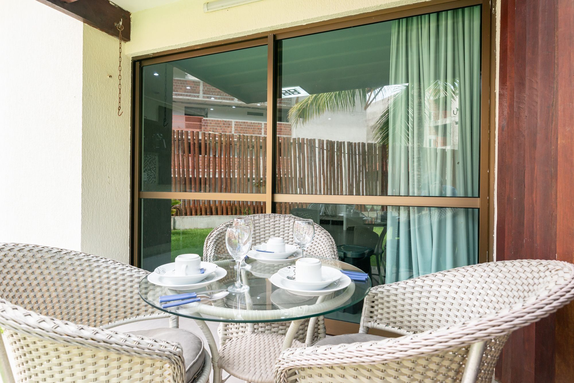 A glass-top table with white plates, cups, and glasses, surrounded by wicker chairs.