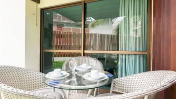A glass-top table with white plates, cups, and glasses, surrounded by wicker chairs.
