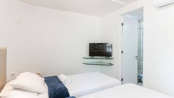 A hotel room with two beds, a television mounted on a glass shelf, and a door leading to a bathroom.