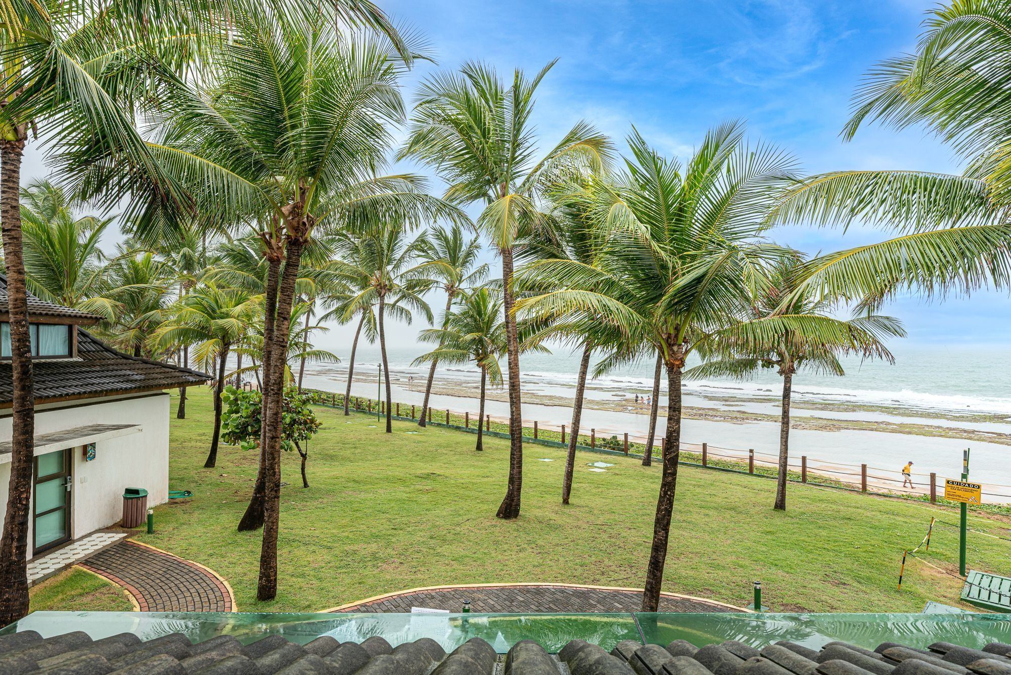 Um imóvel à beira-mar com piscina, palmeiras e vista para o oceano.