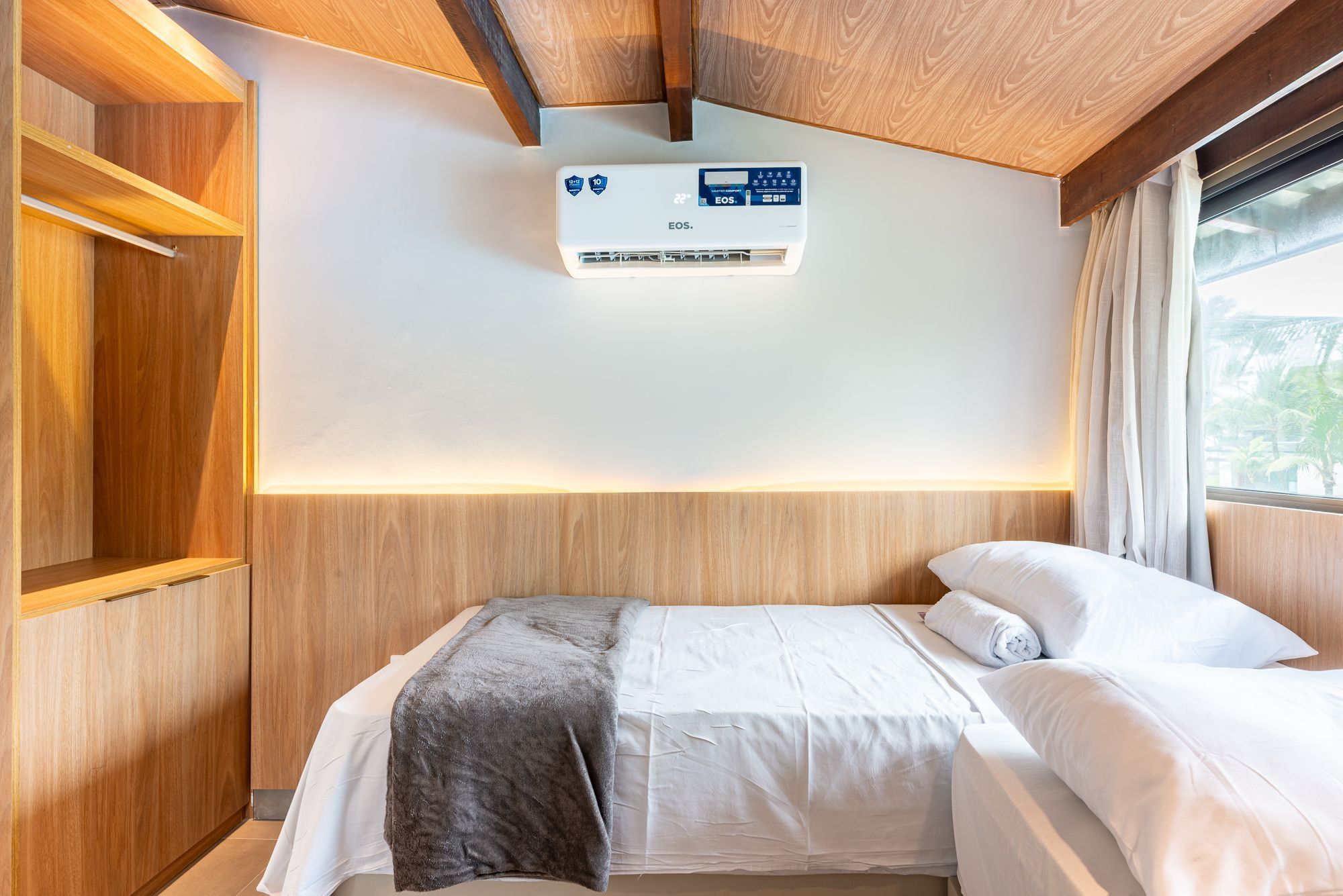 Een hotelkamer met een bed, een wandairconditioner en een raam met gordijnen.