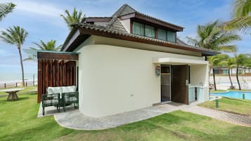 A modern two-story house with a balcony, a pool, and a view of the beach.