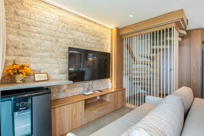 A modern living room with a stone wall, a flat-screen TV, a wooden entertainment unit, a sofa, and a staircase with a rope barrier. - BeachClass Muro Alto Porto de Galinhas (Ipojuca)
