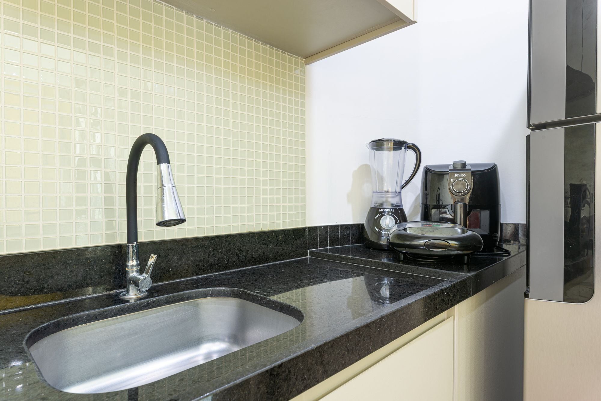 A kitchen with a stainless steel sink, a coffee maker, and a blender on the counter.