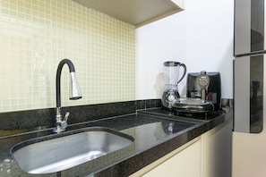 Una cocina con un lavamanos de acero inoxidable, una cafetera y una licuadora sobre la encimera.