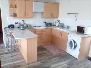 A compact kitchen with a central island, a washing machine, and a microwave. - Charming 1 Bedroom Apartment and Double Sofabed in Milton Keynes (Milton Keynes)