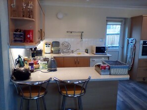 A compact kitchen with a microwave, kettle, and bar stools. - Charming 1 Bedroom Apartment and Double Sofabed in Milton Keynes (Milton Keynes)