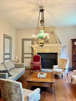 Ein Wohnzimmer mit Kamin, einer Chandelierleuchtre und einem roten Sessel.
