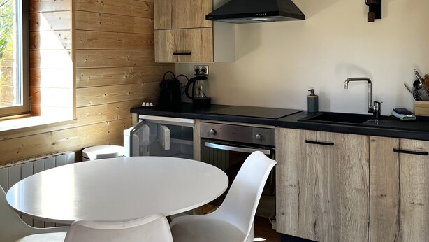 A modern kitchen with wooden cabinetry, a round dining table, and white chairs. - La Petite Cabane (Saint-Affrique)