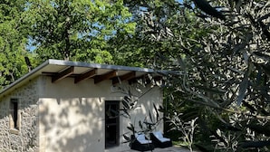A small stone building with a sloped roof, a door, and a window. There are two black lounge chairs outside. - La Petite Cabane (Saint-Affrique)