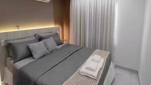Une chambre moderne avec un lit, des tables de chevet, un appareil de climatisation et une grande fenêtre avec des rideaux.